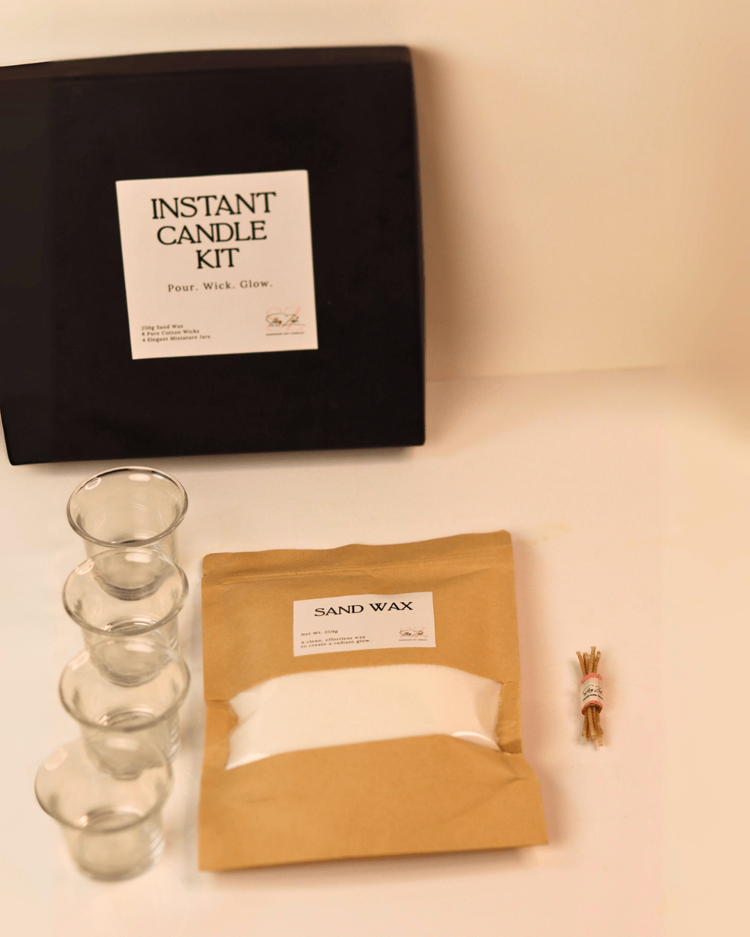 Instant candle kit with black box, glass candle sticks, sand wax, and wick on a beige background